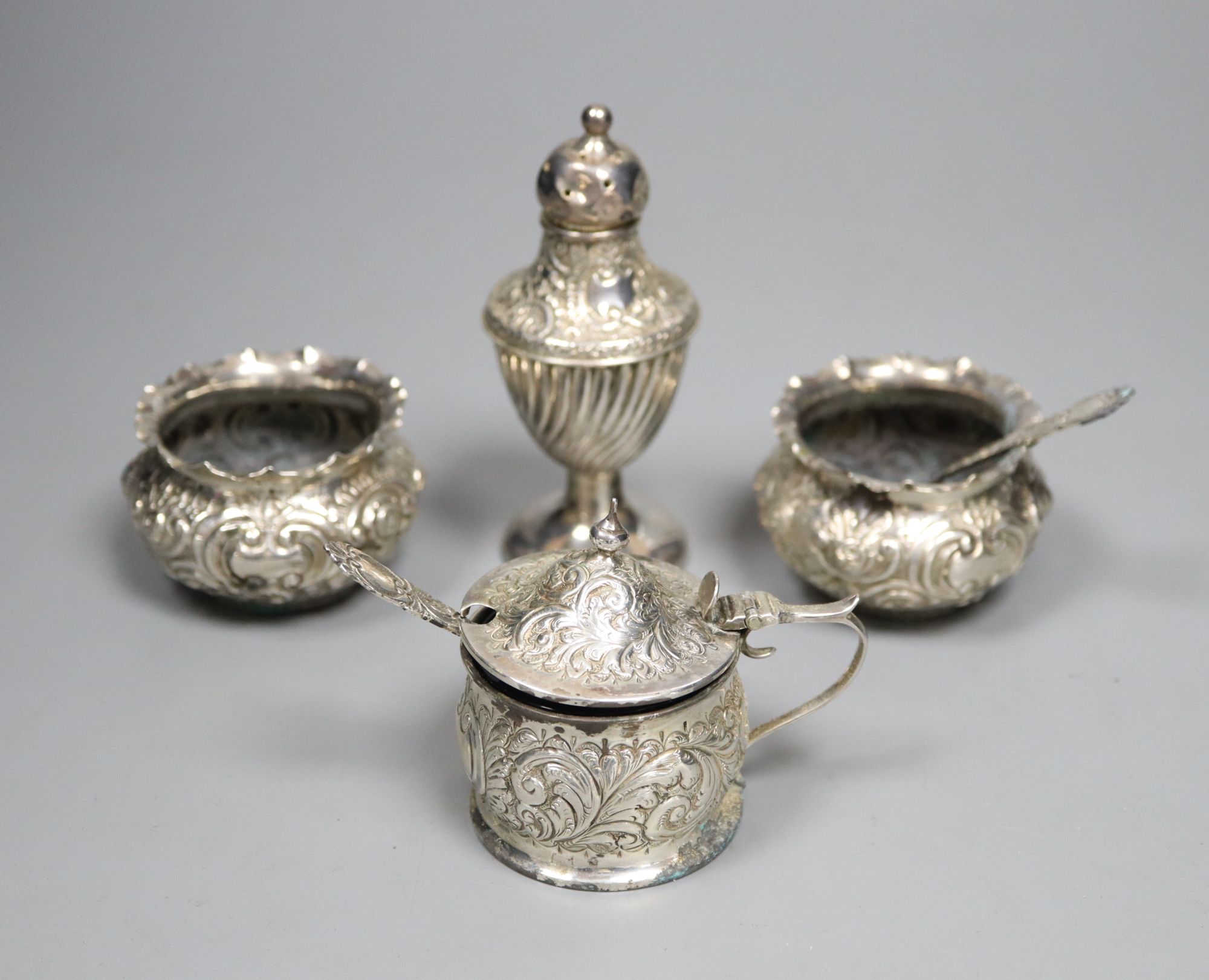 A pair of late Victorian embossed silver salts and one salt spoon, together with a silver mustard pot and a pepper pot (5)